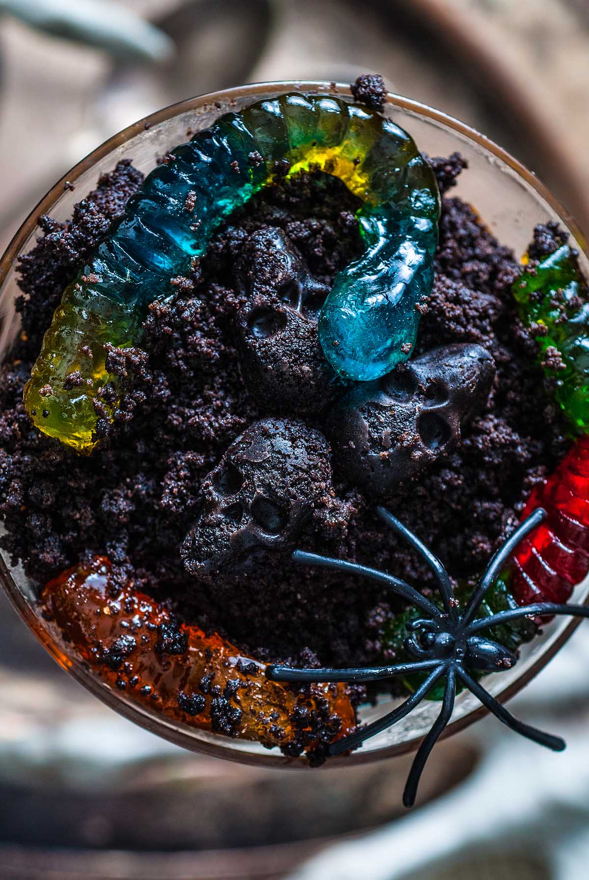 Chocolate pudding “dirt” topped with gummy worms, candy skulls, and a plastic spider makes this Halloween dessert a spooky treat everyone will love.
