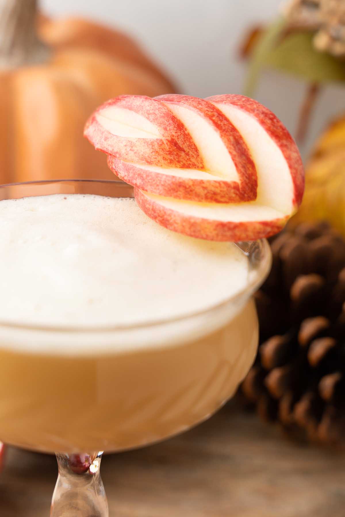 A frothy Maple Apple Whiskey Sour in a glass, garnished with fanned red apple slices.
