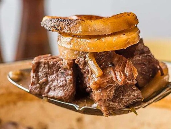 A spoon scooping beef and potatoes.