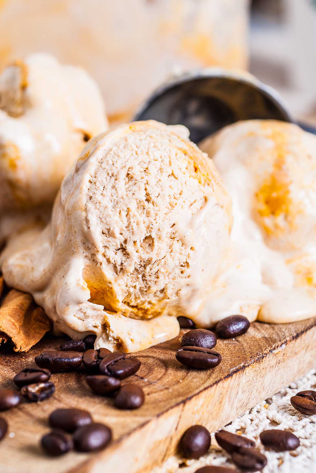 Scoops of creamy no churn pumpkin spice latte ice cream melting on a wooden board, with coffee beans scattered around.