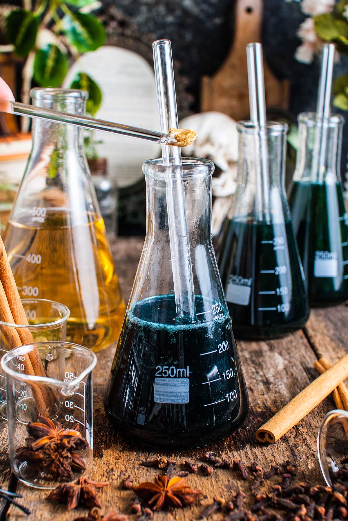 A hand stirs a shimmering Halloween apple cider punch in a 250 ml flask with a glass rod, surrounded by beakers and spices.