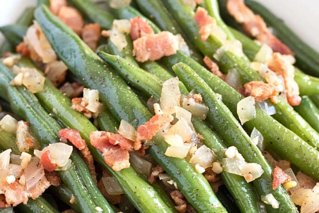 A serving dish of green beans with bacon crumbles over top.