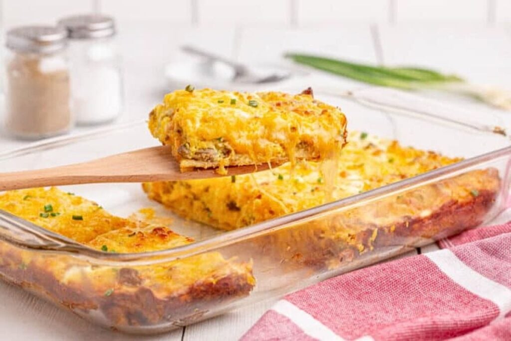 A serving of crescent roll casserole being lifted from the dish with a wooden spatula.
