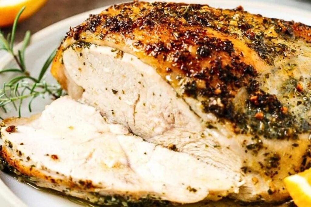 A turkey breast coated with herbs, garlic and butter on a platter.