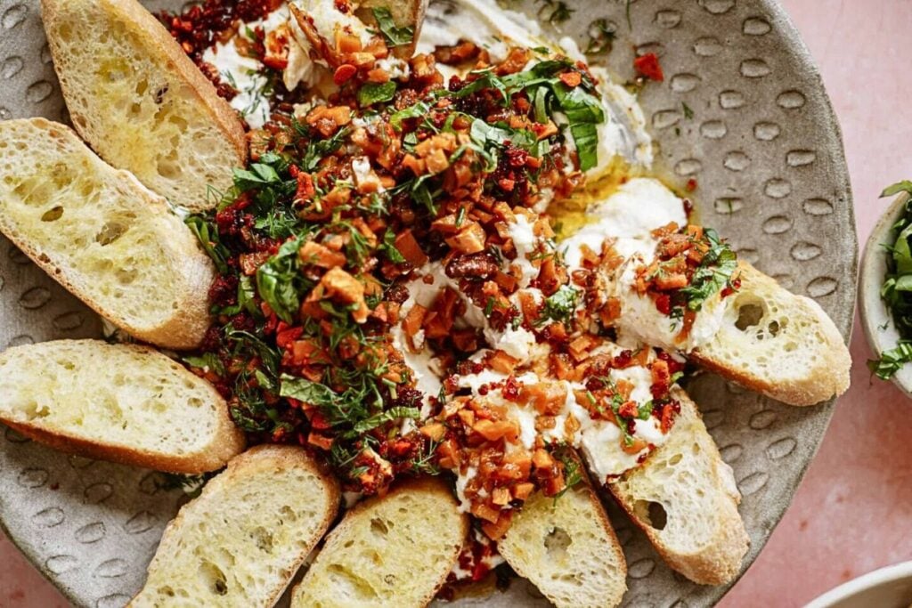 A dish of goat cheese dip topped with maple spiced sweet potato cubes.