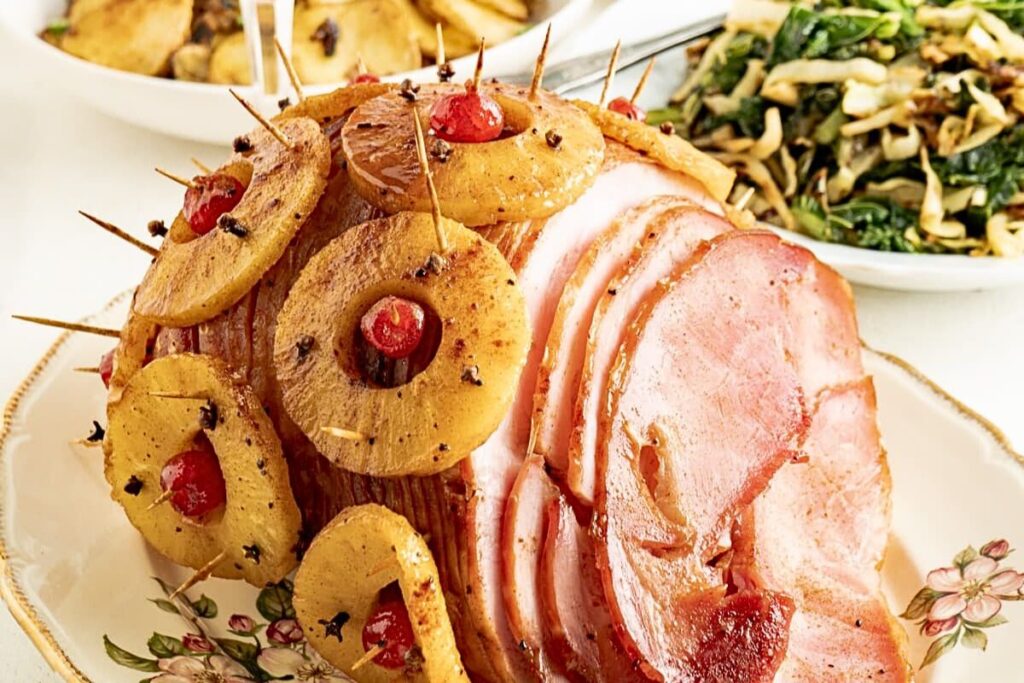 A pineapple and cherry studded ham on a serving platter.