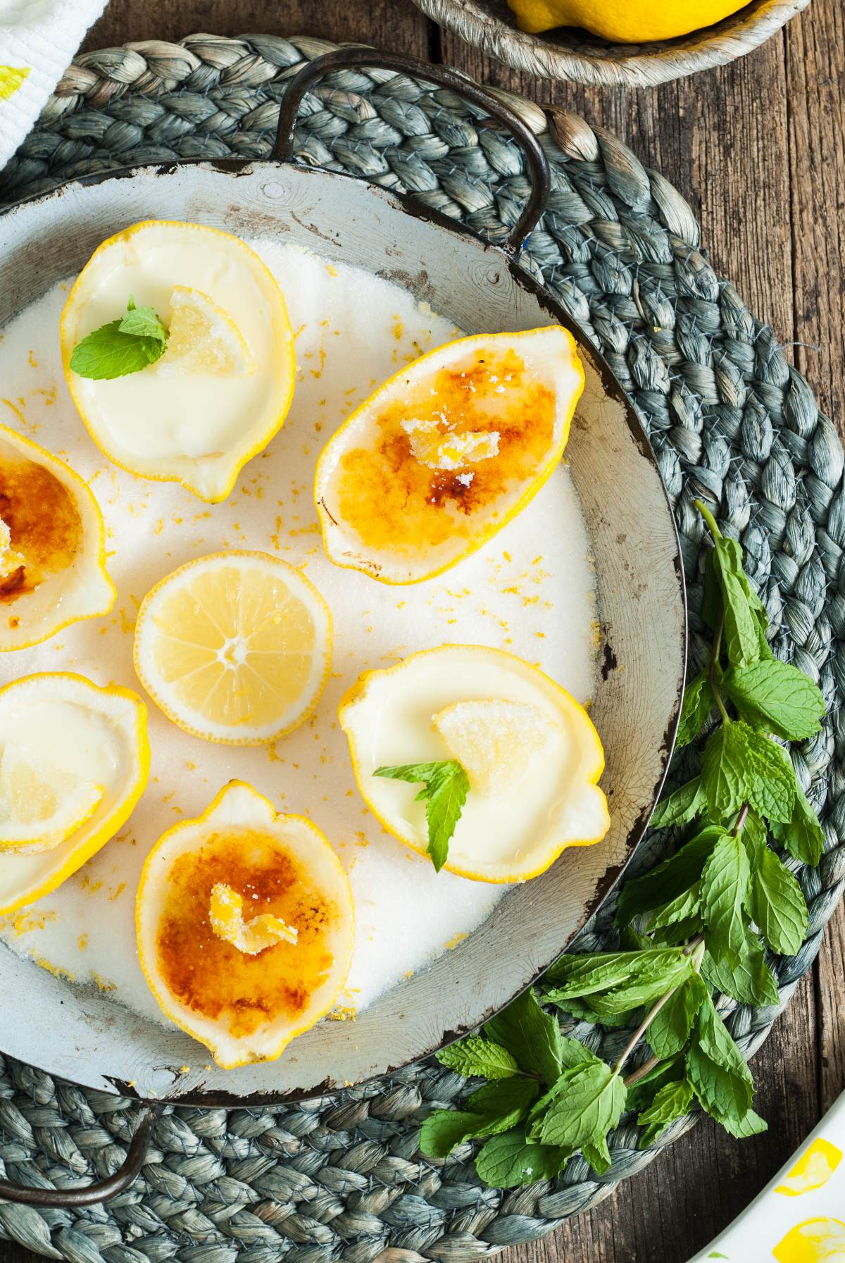 Lemon halves filled with Lemon Posset Brûlée, topped with a caramelized crust, garnished with mint leaves and a lemon slice on a tray.