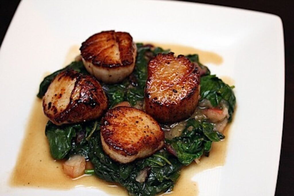 A plate of spinach and seared scallops.