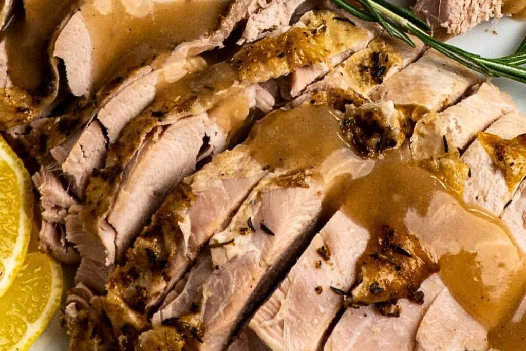 A platter of slow cooked turkey breast with gravy over top.