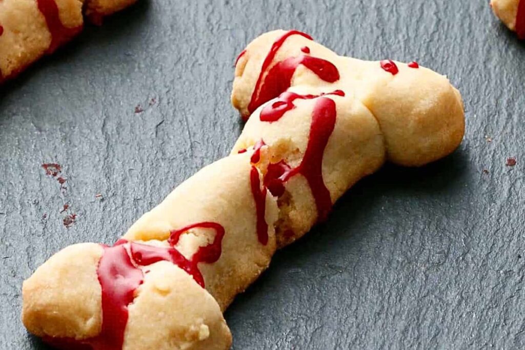 Biscuit cookies shaped like bones, with bloody icing drizzle.