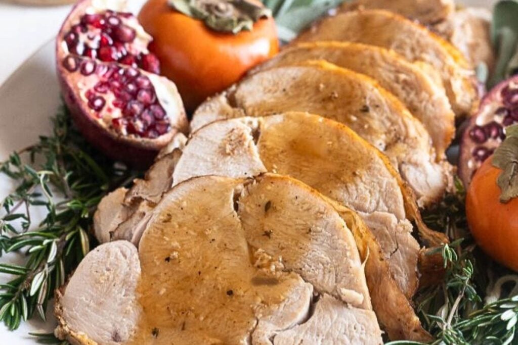 A platter of roasted turkey breast, sliced and drizzled with gravy.