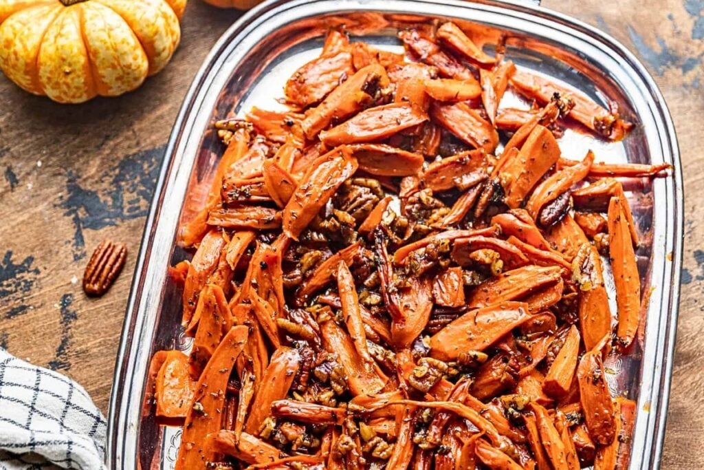 A serving platter of brown sugar glazed carrots, topped with pecans.