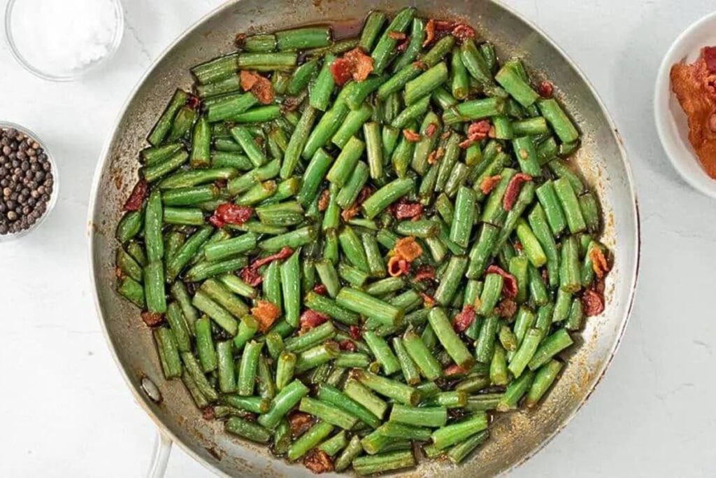 A skillet of green beans with bacon chunks.