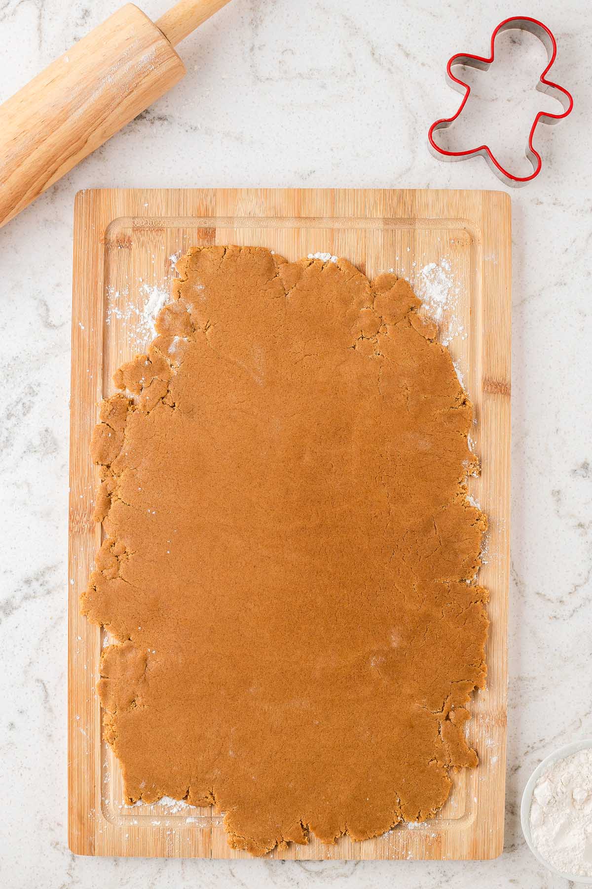 Rolled-out gingerbread dough on a wooden board with a rolling pin and gingerbread cookie cutter nearby, perfect for making Easy Gingerbread Man Cookies.