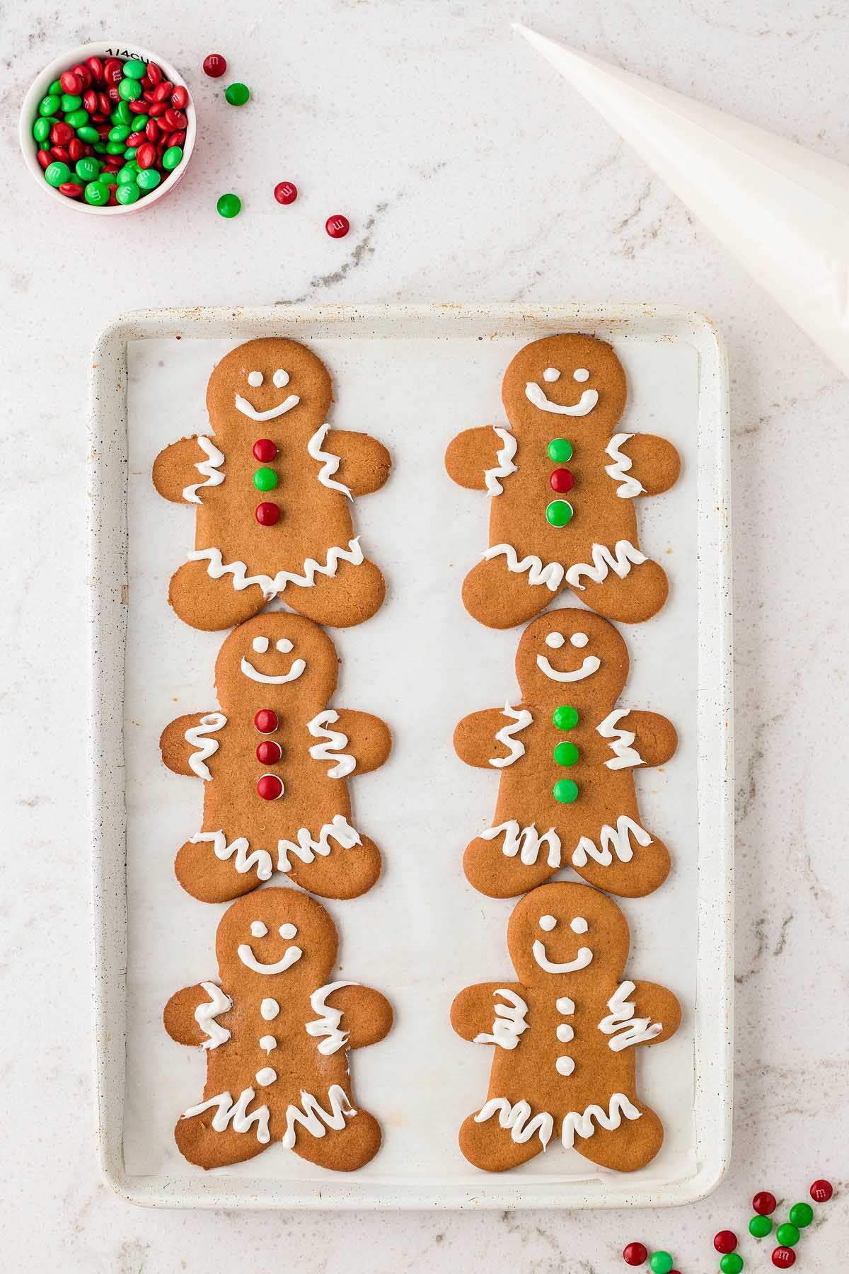 Six decorated Easy Gingerbread Man Cookies on a tray, with red and green candies and a piping bag nearby.