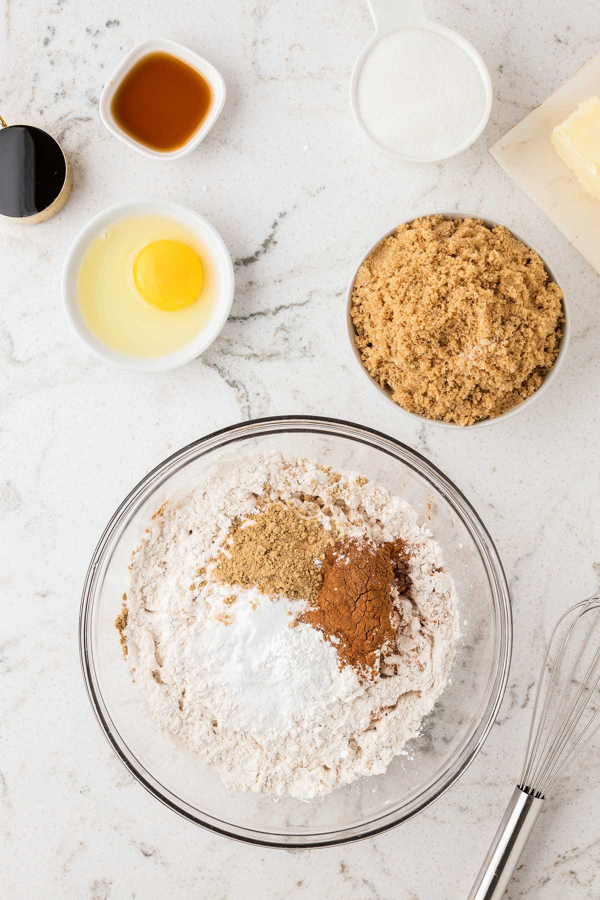 Baking ingredients in bowls, including flour, sugar, brown sugar, spices, butter, an egg, and vanilla on a counter—everything you need to make Easy Gingerbread Man Cookies.