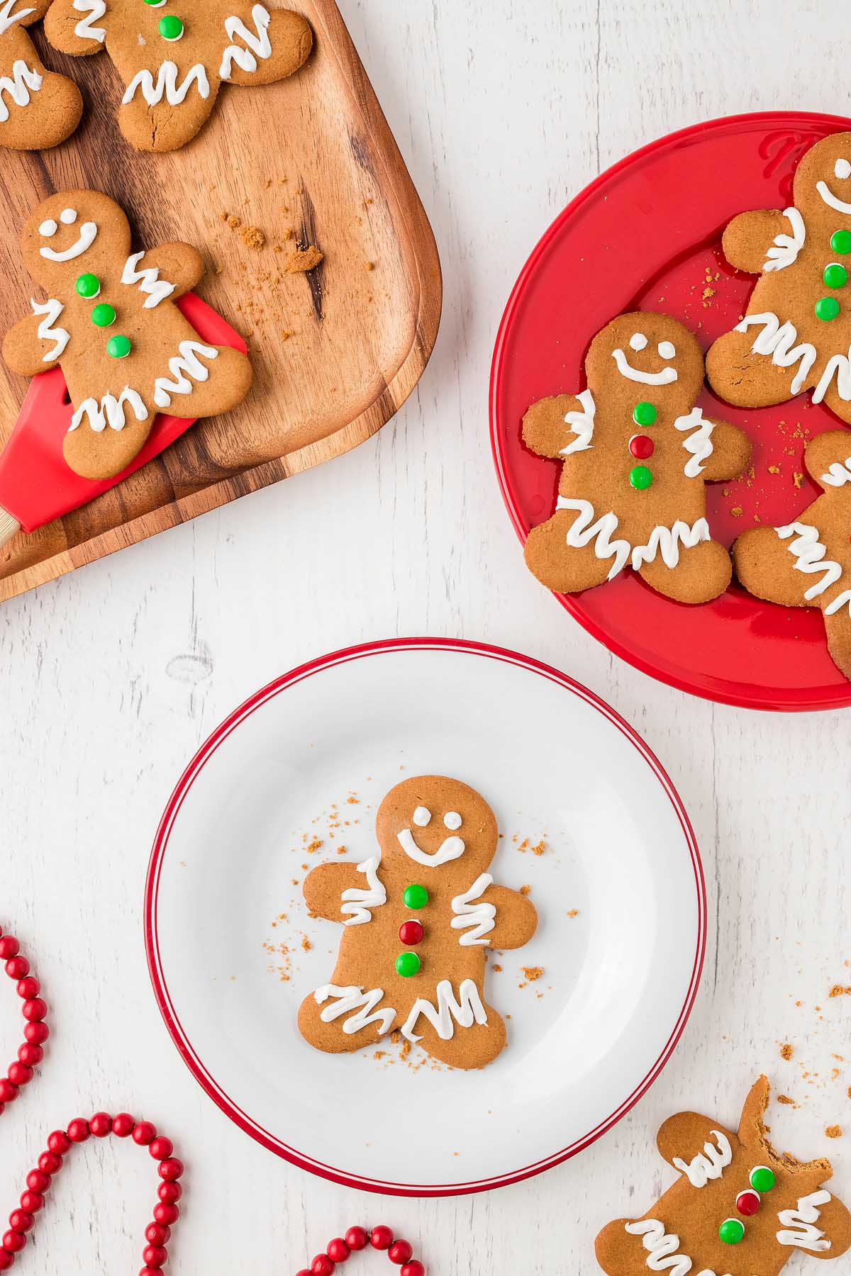 Easy Gingerbread Man Cookies decorated with icing and candy are displayed on plates atop a white wooden table.