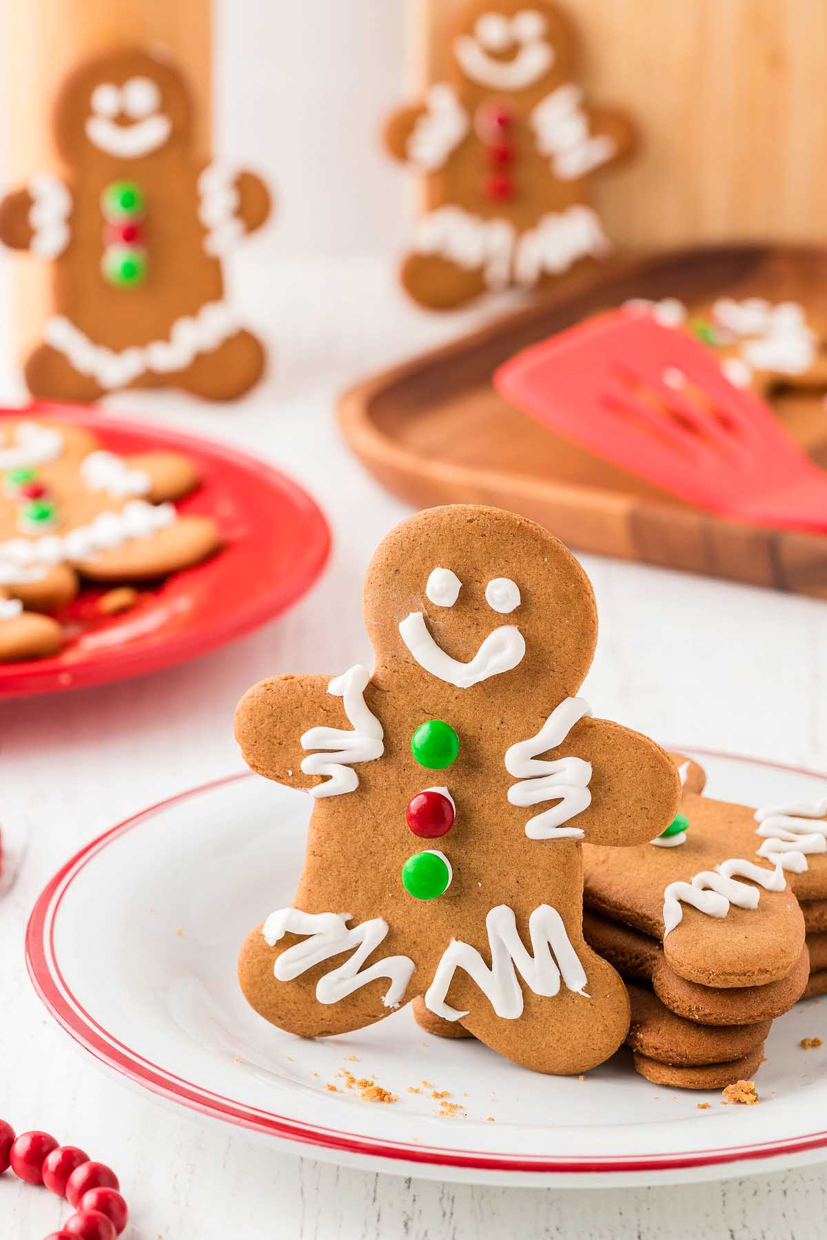 A smiling gingerbread cookie with icing and candy buttons on a plate, showcasing the fun and charm of Easy Gingerbread Man Cookies, with more cookies in the background.