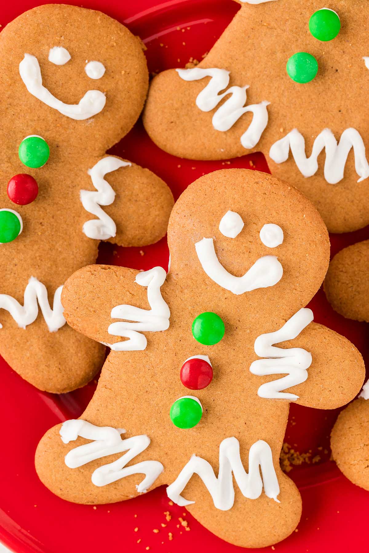 Easy Gingerbread Man Cookies decorated with white icing and red and green candies are arranged on a festive red plate.