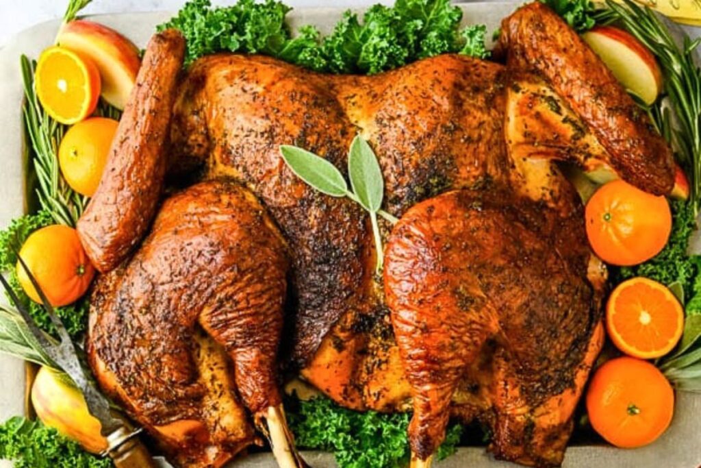A spatchcock grilled turkey on a platter with citrus fruit.