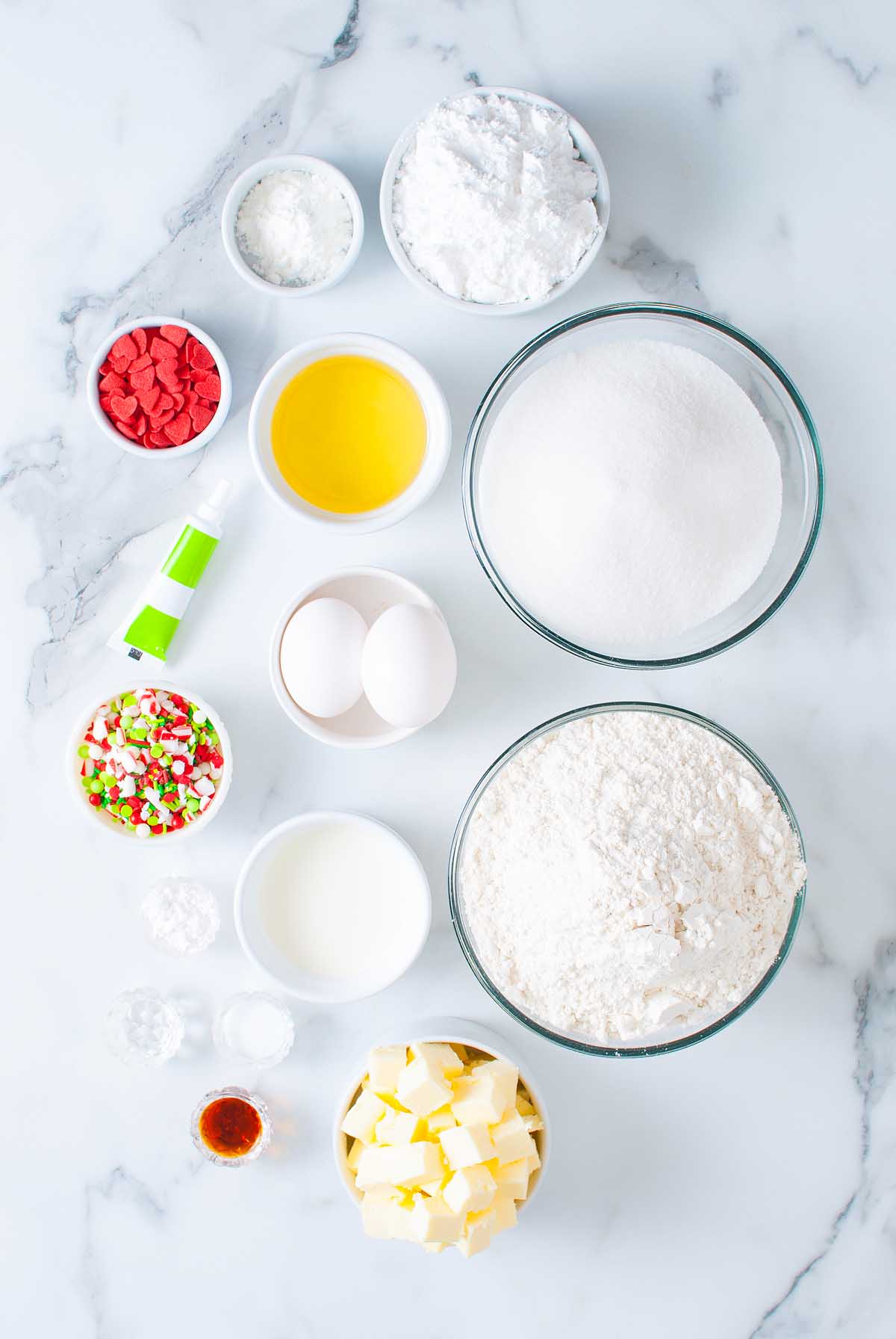 Baking ingredients in bowls: flour, sugar, eggs, butter, oil, milk, sprinkles, food coloring, and baking powder—perfect for making festive Grinch Crumbl Christmas Sugar Cookies.