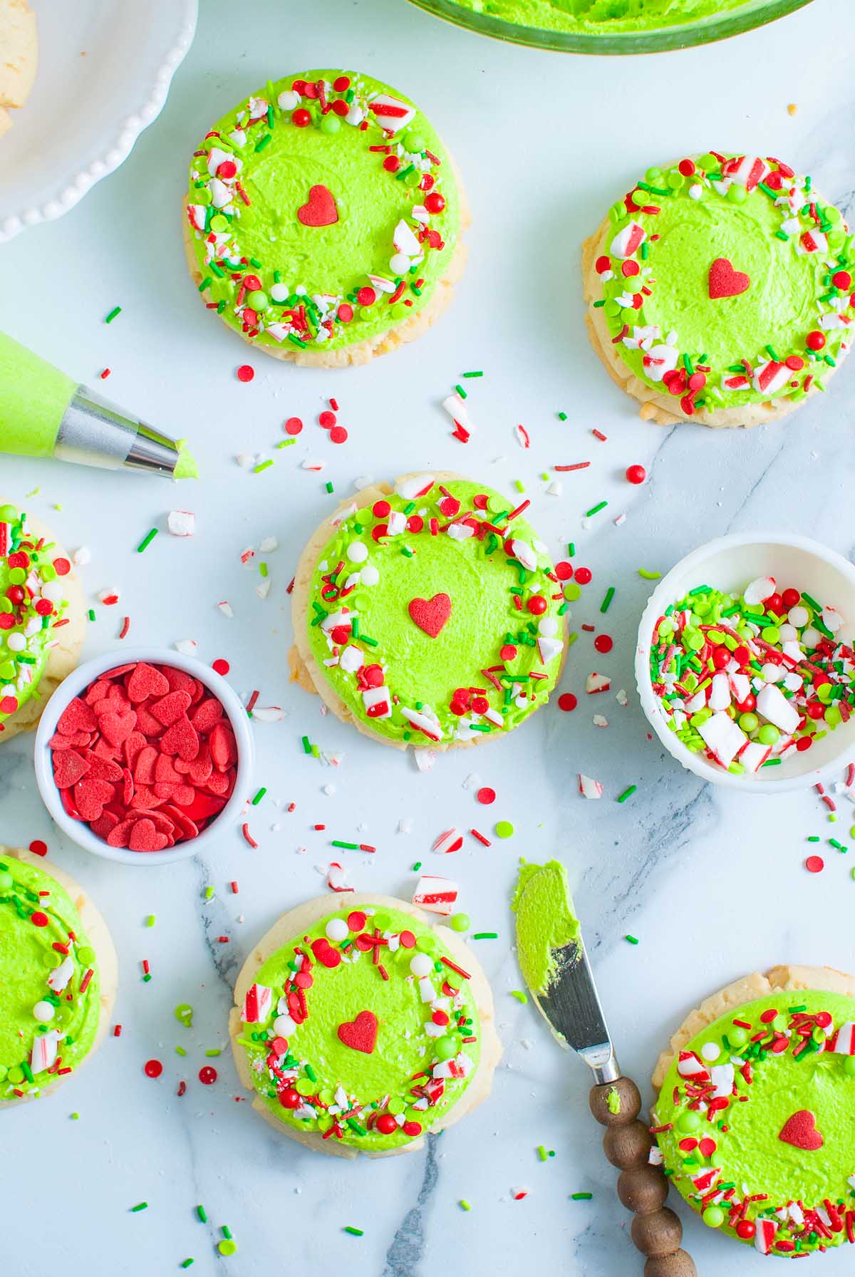 Round Grinch Crumbl Christmas Sugar Cookies with bright green frosting, red heart sprinkles, and festive red, white, and green toppings.