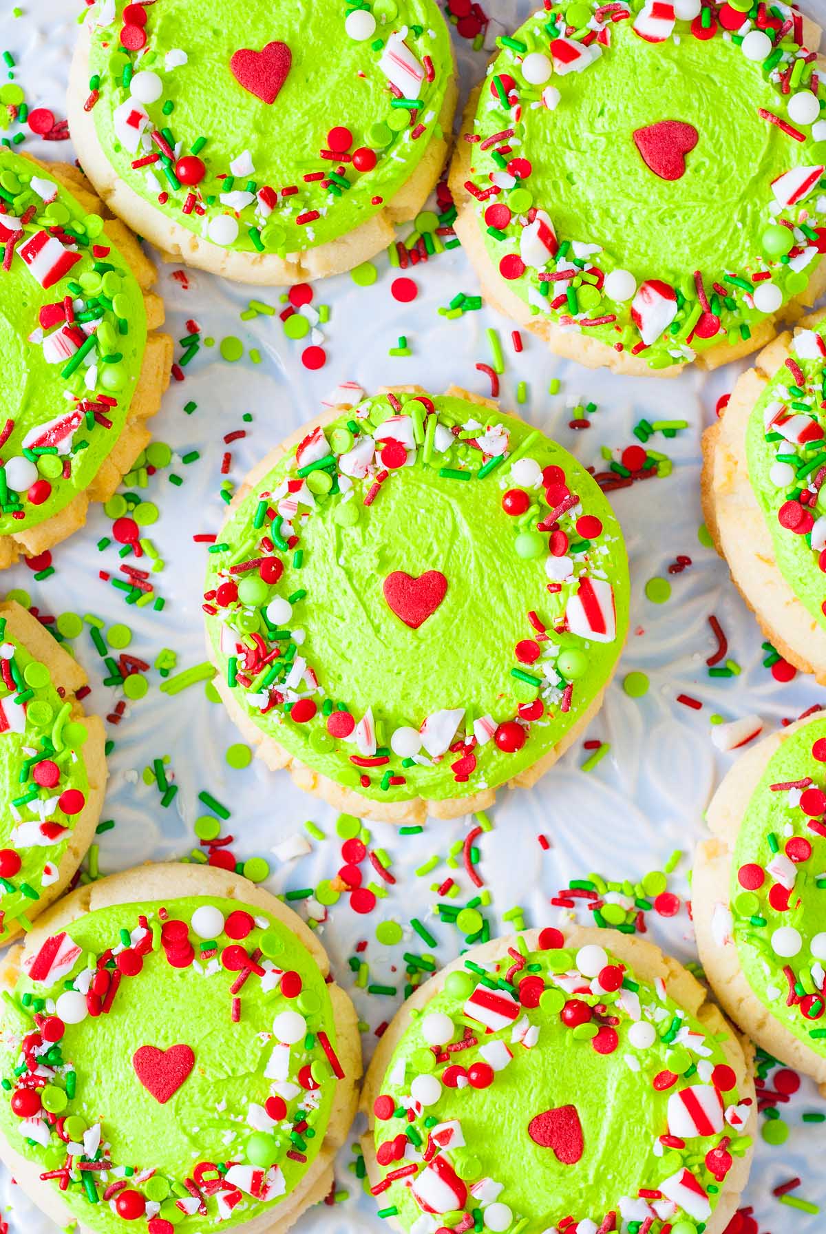 Round Grinch Crumbl Christmas sugar cookies with bright green icing, red heart centers, and festive red, white, and green sprinkles.
