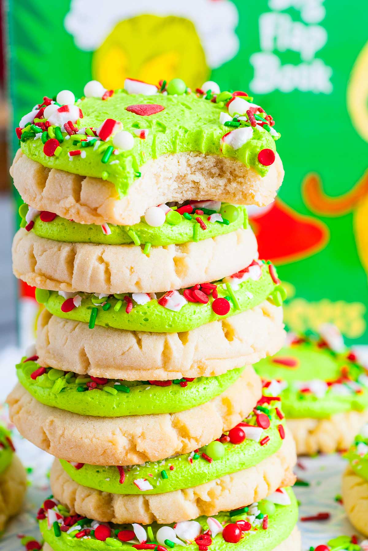 A stack of Grinch Crumbl Christmas Sugar Cookies with green frosting and festive red, white, and green sprinkles.