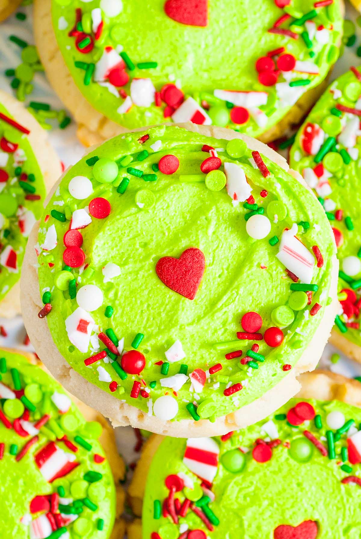 Grinch Crumbl Christmas Sugar Cookies topped with bright green frosting, red heart candies, and festive red, white, and green sprinkles.