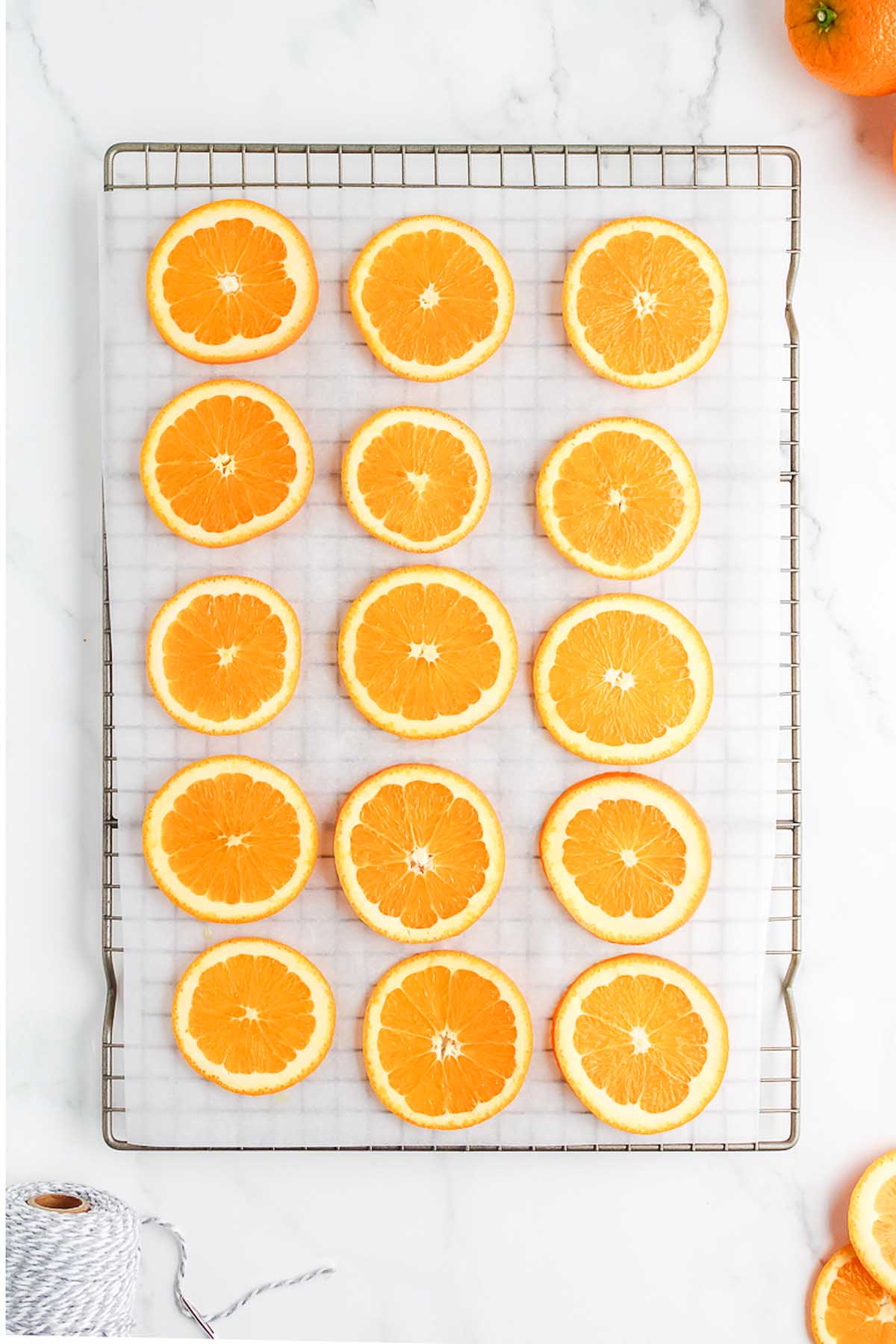 Sixteen orange slices arranged in neat rows on a wire rack lined with parchment paper, ready to become a beautiful Homemade Dried Orange Garland.