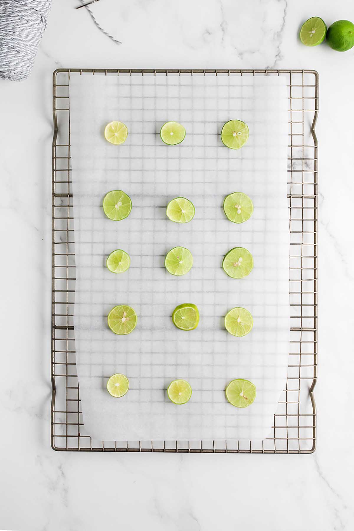 Slices of lime are arranged on parchment paper placed on a cooling rack, perfect for pairing with a Homemade Dried Orange Garland on a white surface.