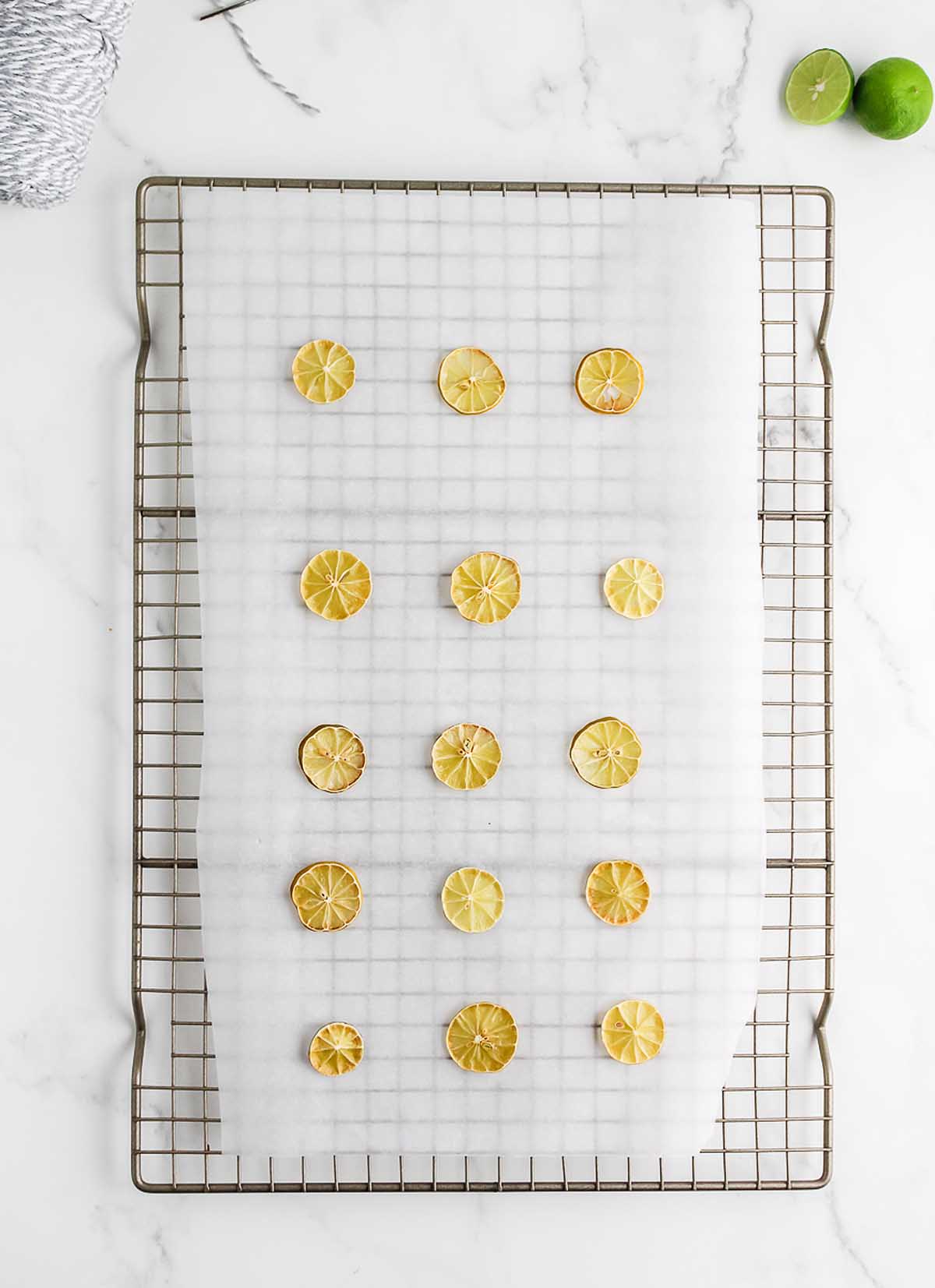 Lime slices arranged on parchment paper over a cooling rack, with a halved lime nearby&mdash;perfect inspiration for crafting a Homemade Dried Orange Garland.