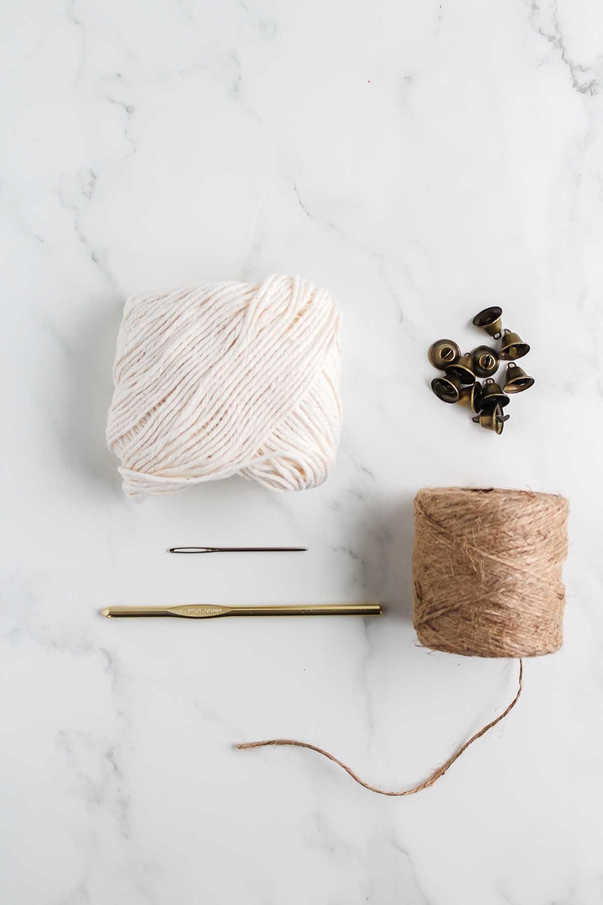 Yarn, jute twine, a crochet hook, a needle, and buttons arranged on a white marble surface—everything you need for How to Make a Crochet Star Garland.