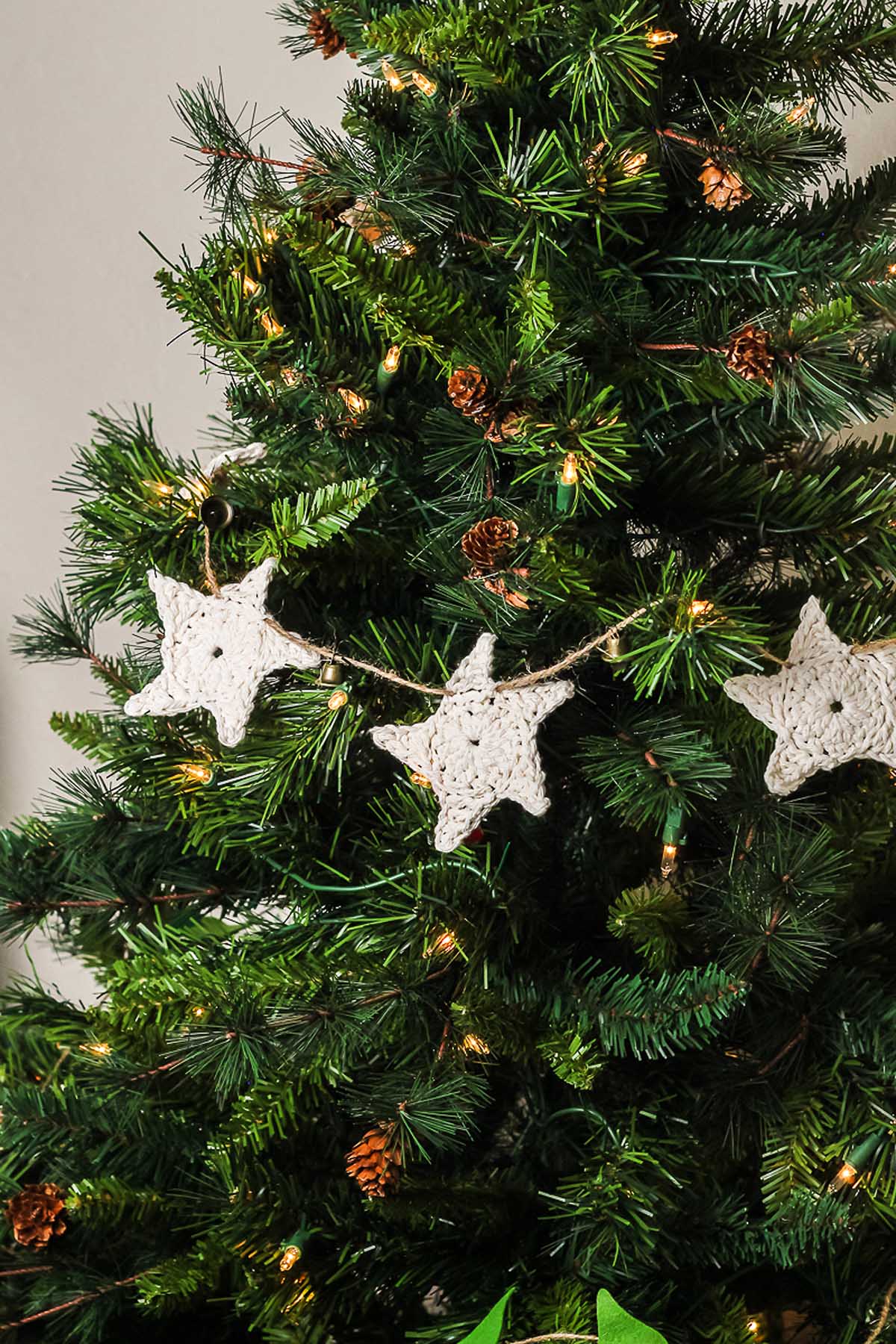 Christmas tree decorated with white crocheted star garland, pinecones, and string lights—perfect inspiration if you’re wondering how to make a crochet star garland for your own festive decor.