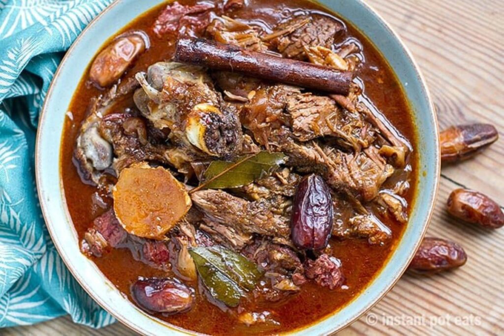 A bowl of stew with leg of lamb, dates and cinnamon sticks.