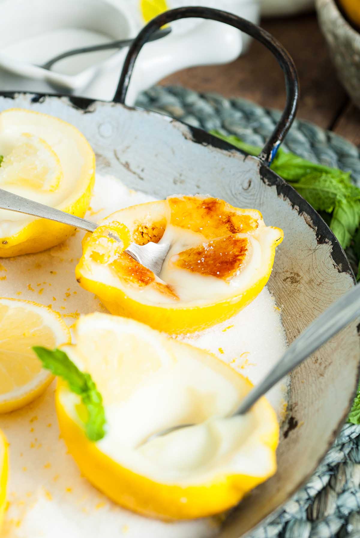 Lemon Posset Brûlée: Lemon halves filled with creamy dessert, topped with caramelized sugar and served with spoons.