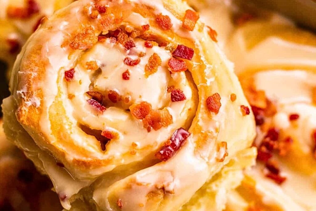 Maple bacon cinnamon rolls in a casserole dish, with one roll being lifted out.
