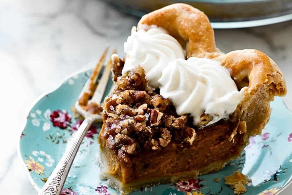 Pumpkin pie with pecan praline topping, sliced on a plate.