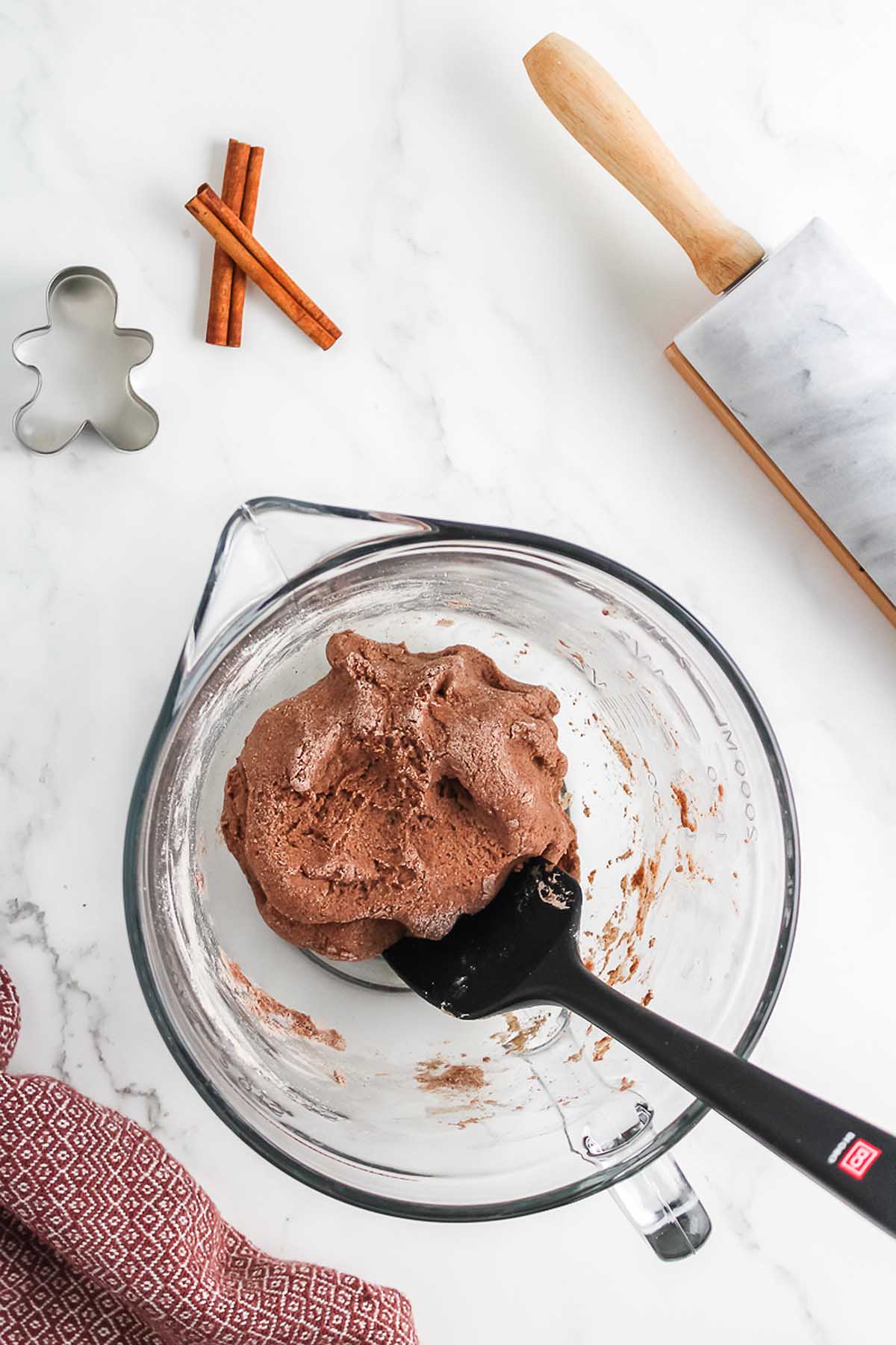 Glass bowl with chocolate cookie dough, black spatula, rolling pin, cinnamon sticks, and a gingerbread cutter&mdash;perfect for crafting a Salt Dough Gingerbread Man Garland or baking festive holiday treats.