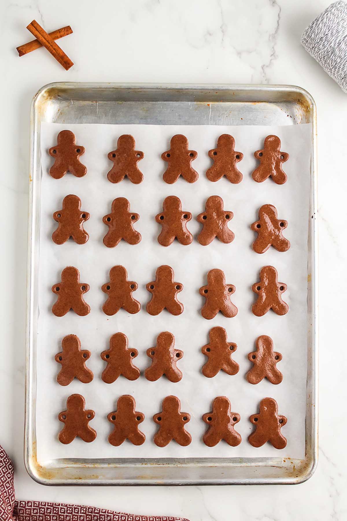 A baking tray with rows of Salt Dough Gingerbread Man Garland cookies shaped like little people on parchment paper.