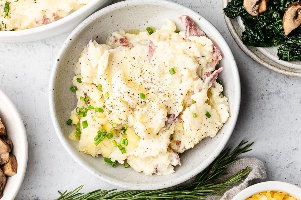 A bowl of red mashed potatoes with gouda cheese.