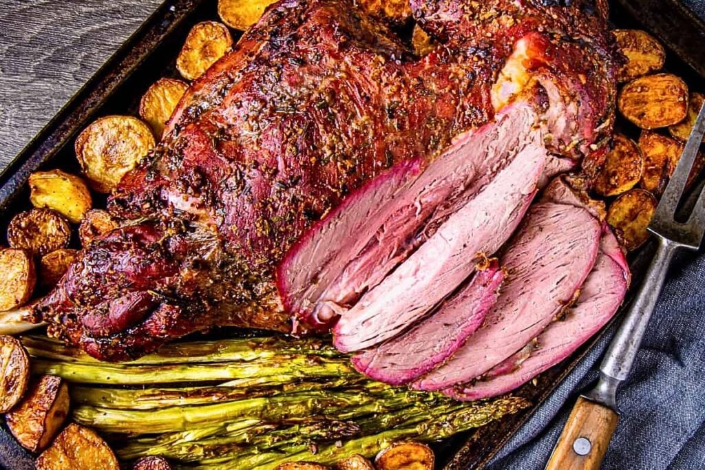 A baking sheet of leg and lamb with potatoes and asparagus on the side.