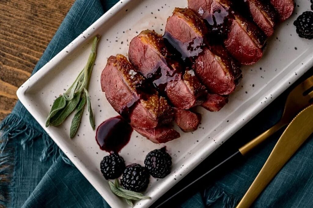 A platter of duck breast with blackberry sage sauce.