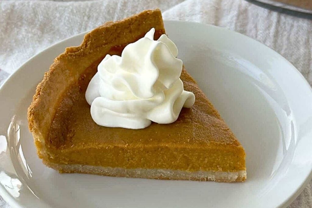 A slice of homemade sweet potato pie on a plate, with whipped cream.
