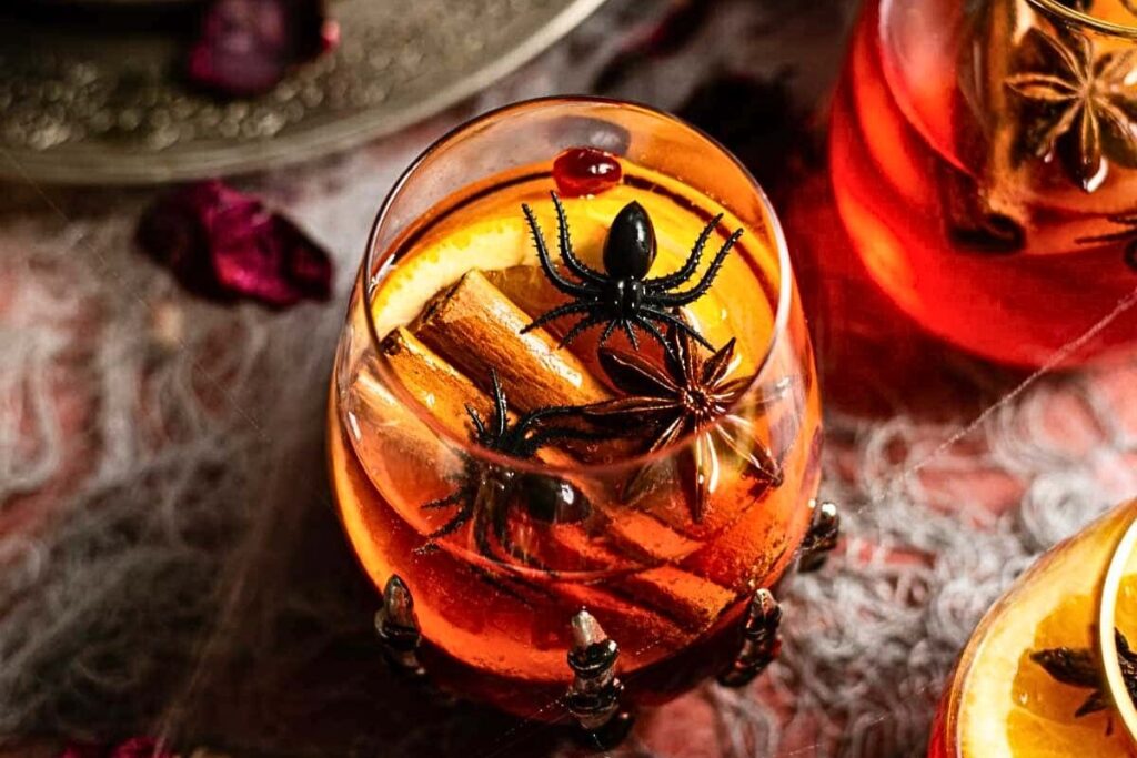 A processeco party punch, in a stemless glass, with spiders crawling over.