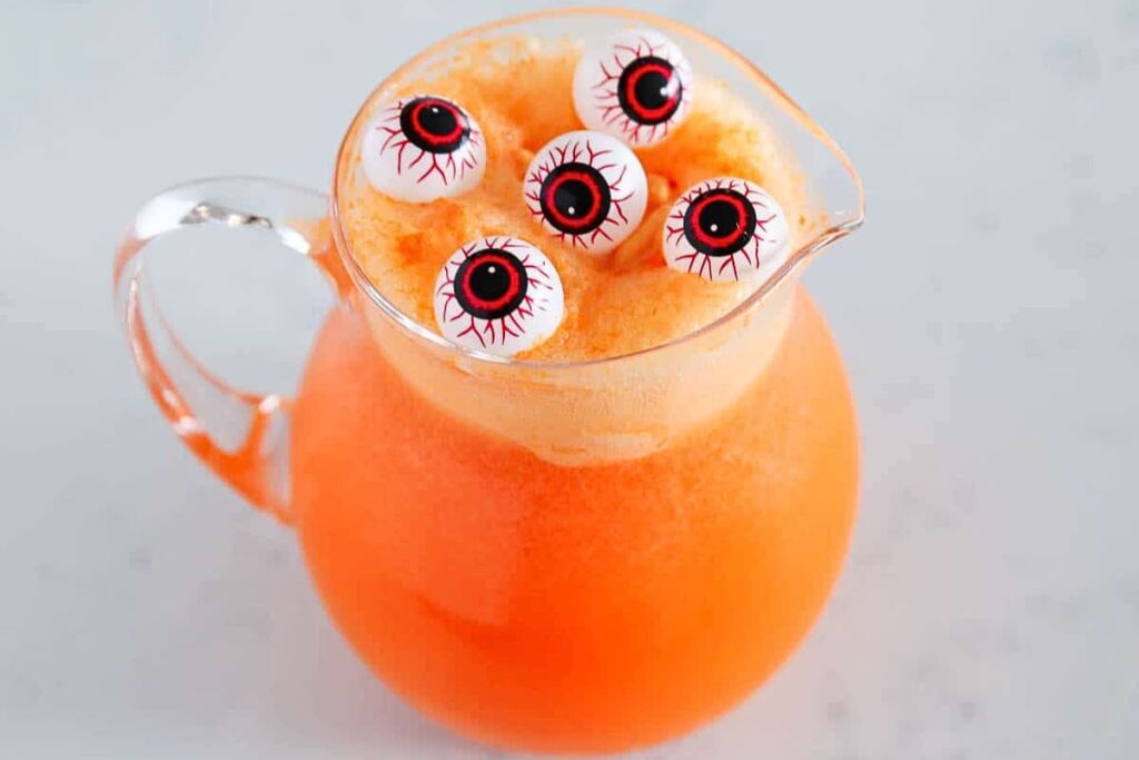 A pitcher of orange punch with eyeball decorations.