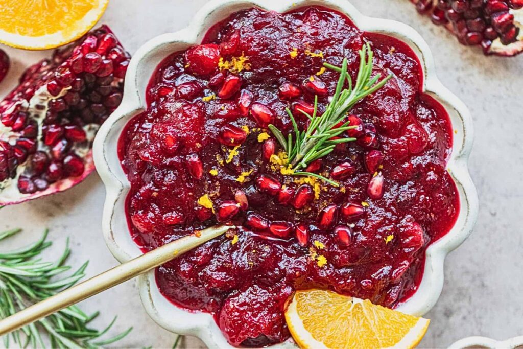 A dish of pomegranate cranberry sauce with a sprig rosemary.