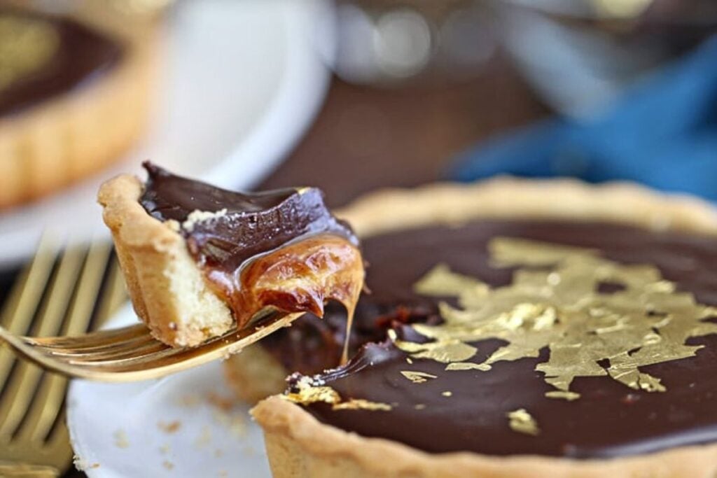 A gooey chocolate caramel tart with a bite being lifted away.
