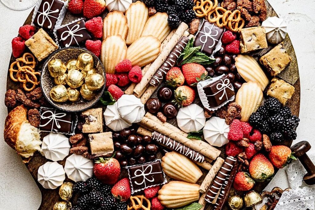 A charcuterie board filled with fruit, candy and cookies.