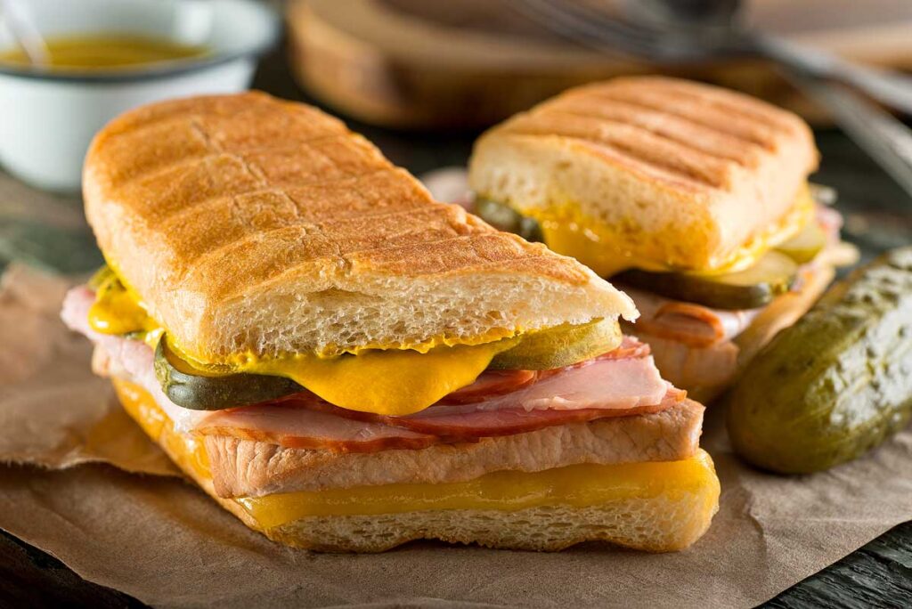 An authentic cuban sandwich on pressed medianoche bread with pork, ham, cheese, pickle, and mustard.